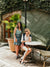 Two women sitting at a table outdoors with a stone wall and potted plant in the background. | Lifestyle